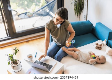 Busy mother talking on the phone while babysitting her daughter and working on a laptop from home. - Powered by Shutterstock