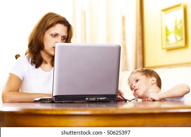 busy mother works on a laptop while ignoring her child