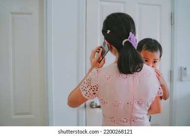 A Busy Multitasking Mom, Asian Mom With Baby Talking On Mobile Phone And Using Computer For Working From Home While Take Care Baby At Home. Woman Busy With Urgent Work At Home. Due To Covid19 Virus Pa