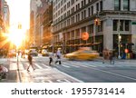 Busy New York City scene with crowds of people and cars in the intersection of Fifth Avenue and 23rd Street in Midtown Manhattan with the light of sunset in the background