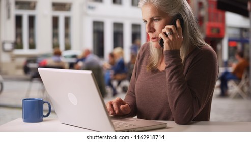 Busy Older White Woman Works From Laptop And Makes Phone Call At Cafe