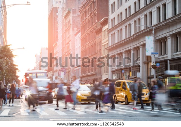 Busy people in motion\
across an intersection on Broadway in New York City with sunlight\
background