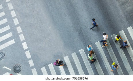 Busy people walk on the pedestrian crosswalk at traffic road with the signage on the city road (Aerial photo, top view)