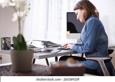 Busy Pretty Young Businesswoman in Denim Blouse Sitting at her Worktable with Documents and Electronic Devices. - Powered by Shutterstock