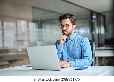 Busy professional business man company employee, young male worker software developer, latin businessman looking at computer thinking on online investment management using laptop working at office.