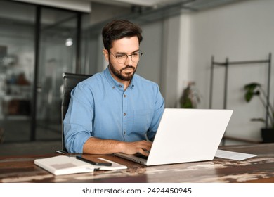 Busy professional business man company employee, young male worker software developer, latin businessman typing on computer technology using laptop searching on web working at office workplace desk.