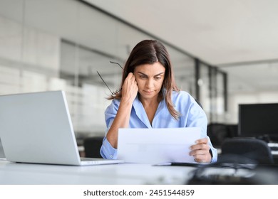 Busy professional mature business woman reading bad news in document at work. Worried serious middle aged businesswoman entrepreneur looking at paper bill sitting at desk in office. - Powered by Shutterstock