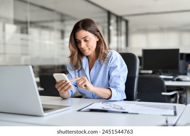 Busy professional middle aged business woman using mobile phone working in office. Smiling mature businesswoman executive holding cell at desk. Happy female worker making bank payments on smartphone. - Powered by Shutterstock