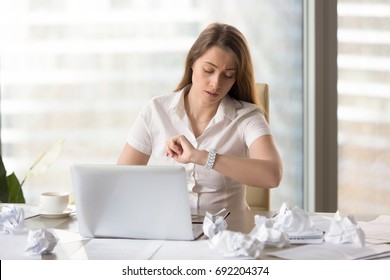 Busy punctual businesswoman checking time to deadline, looking at wristwatch while working with laptop and documents, need to finish work on time, counting on overtime bonus, waiting workday ending