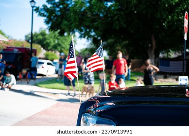 Busy residential road intersection with blurred diverse group of people watching July Fourth parade, lawn flags display front of modern pickup truck smalltown in Dallas, Texas, USA. Independence Day
