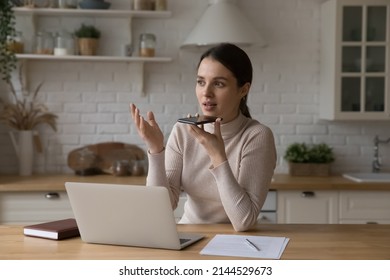 Busy Serious Freelance Professional Woman Talking On Speaker On Smartphone At Home Workplace. Business Woman, Entrepreneur, Remote Employee Giving Voice Command To Virtual Assistant On Cell