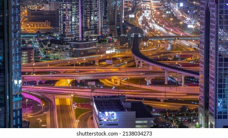 Busy Sheikh Zayed Road Intersection Aerial Night Timelapse, Metro Railway And Modern Skyscrapers Around In Luxury Dubai City. Heavy Traffic On A Highway Junction With Many Cars. United Arab Emirates