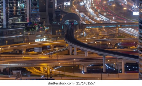 Busy Sheikh Zayed Road Junction Aerial Night Timelapse, Metro Railway And Modern Skyscrapers Around In Luxury Dubai City. Heavy Traffic On A Highway Crossroad With Many Cars. United Arab Emirates