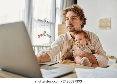 busy single father holding his cute infant son in hands while working from home, work-life balance - Powered by Shutterstock