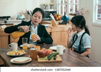 Busy Single Mom In Business Suit Before Work In Morning Prepared Handmade Healthy Meal. Young Woman Mother Pour Fresh Orange Juice In Glasses For Daughter Eating Breakfast Before School. Family Time.