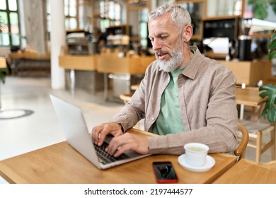 Busy Smart Mature Professional Business Man Using Laptop Sitting In Cafe. Middle Aged Older Adult Businessman, Senior Entrepreneur Of Mid Age Remote Working Or Learning Online Typing On Computer.