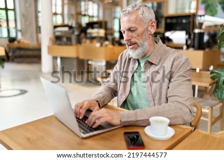 Busy smart mature professional business man using laptop sitting in cafe. Middle aged older adult businessman, senior entrepreneur of mid age remote working or learning online typing on computer.