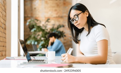 Busy smart young asian girl student marketing smm manager social media worker freelancer intern businesswoman working remote distant studding in office desk in coworking space. College education - Powered by Shutterstock