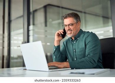 Busy smiling older middle aged business man professional expert or entrepreneur making phone call speaking with client communicating on cellphone using laptop computer sitting at desk in office. - Powered by Shutterstock