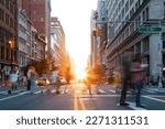 Busy street scene is crowded with people at an intersection on Fifth Avenue in New York City with sunlight shining between the background buildings