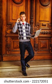 Busy Student. Wearing A Patterned Sweater, Red Tie, Blue Jeans, Leather Shoes, A Young Guy Is Waling Down From Office, Talking On His Mobile Phone, Working On A Laptop Computer In The Same Time. 