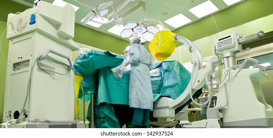 Busy Surgery Room In Hospital, Doctors In Medical Uniforms Operating On Patient