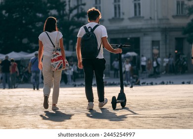 In a busy urban setting, a couple walks side by side in the backlit sunlight with an electric scooter, which is a testament to eternal love and partnership in the busy rhythm of the city - Powered by Shutterstock