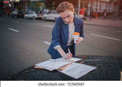 Busy woman is in a hurry, she does not have time, she is going to talk on the phone on the go. Businesswoman doing multiple tasks On the hood of the car. Multitasking business person.