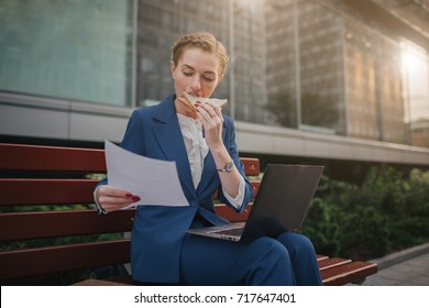 Busy Woman Is In A Hurry, She Does Not Have Time, She Is Going To Eat Snack On The Go. Worker Eating And Talking On The Phone At The Same Time. Multitasking Business Person.