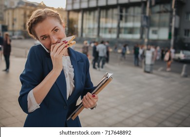 Busy Woman Is In A Hurry, She Does Not Have Time, She Is Going To Eat Snack On The Go. Worker Eating And Talking On The Phone . Businesswoman Doing Multiple Tasks.   Business Female Person.