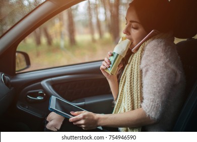 Busy woman is in a hurry, she does not have time, she is going to eat snack on the go. Worker eating and talking on the phone at the same time. She multitasking while eating and working on a tablet PC