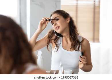 Busy Woman Talking On Phone And Applying Mascara On Eyelashes In A Hurry Being Late For Work Standing Near Mirror In Modern Bathroom At Home. Always In Touch. Selective Focus - Powered by Shutterstock