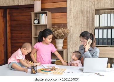 Busy Woman Trying To Work While Babysitting Three Kids.  Young Asian Mother On A Call With Three Children Playing Around Her . Working Women With Multitasking.