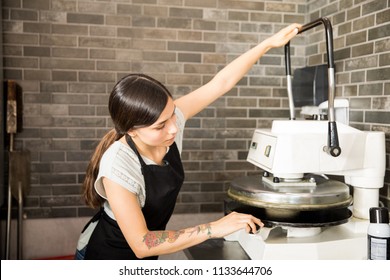 Busy Woman Wearing Black Apron Concentrating On Using Dough Press Machine To Make Pizza Bread In Kitchen At Pizza Shop