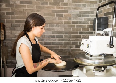 Busy Woman Wearing Black Apron Concentrating On Keeping Dough On Press Machine To Make Pizza Bread In Kitchen At Pizza Shop