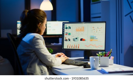 Busy woman working at night in front of computer taking notes writing on notebook annual reports, checking financial project. Focused employee using technology network wireless doing overtime for job