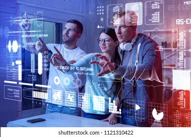 Busy Workers. Clever Professional Web Developers Standing Together And Carefully Touching A Holographic Screen While Working In Their Modern Office