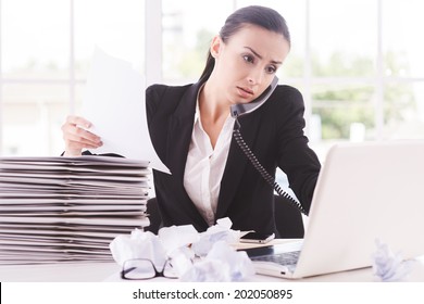 Busy working. Confident young woman in formalwear with documents and talking on the telephone while sitting at her working place