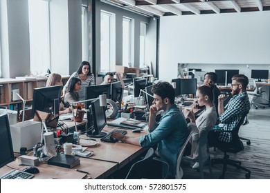 Busy Working Day. Group Of Young Business People Concentrating At Their Work While Sitting At The Large Office Desk In The Office Together