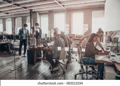 Busy working day in office. Group of young business people working and communicating together in creative office - Shutterstock ID 583521034
