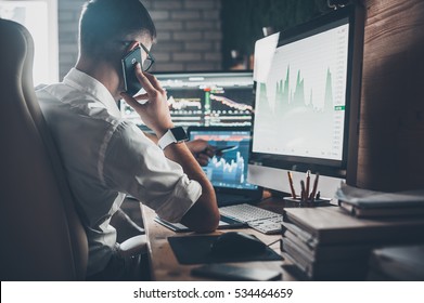 Busy Working Day At Work. Rear View Of Young Man In Casual Wear Talking On The Phone And Working While Sitting At The Desk In Creative Office