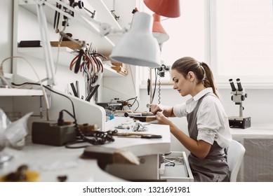 Busy working. Side view of young female jeweler working on a new jewelry product at her workbench. Jewelry making process.