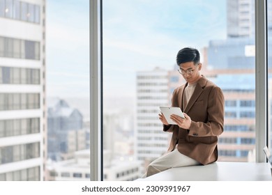 Busy young adult Asian business man professional manager, company executive using digital tablet fintech smart tech device in corporate modern office with big window, copy space, authentic shot. - Powered by Shutterstock