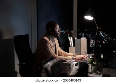 Busy Young African Man Typing On Computer Keyboard And Looking At Screen While Working Late In Office