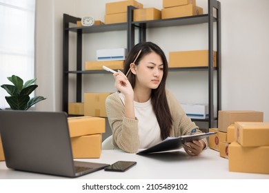 Busy Young Asian Entrepreneur Woman Checking Product On Stock Take Note With Clipboard. Business Woman Working SME Online At Home. Small Business Owner Start Up Freelance Concept.