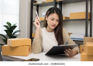 Busy Young Asian Entrepreneur Woman Checking Product On Stock Take Note With Clipboard. Business Woman Working SME Online At Home. Small Business Owner Start Up Freelance Concept.