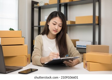 Busy Young Asian Entrepreneur Woman Checking Product On Stock Take Note With Clipboard. Business Woman Working SME Online At Home. Small Business Owner Start Up Freelance Concept.