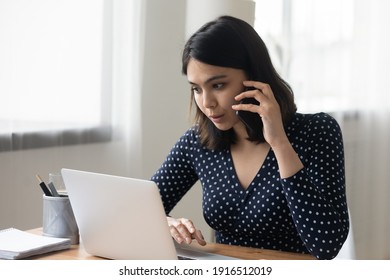 Busy Young Asian Woman Work At Home Office Engaged In Multitask Make Phone Call Check Information Online Using Laptop. Skilled Vietnamese Female Agent Advisor Consult Client By Cell Look At Pc Screen