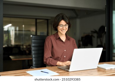 Busy young business woman executive using laptop in office. Smiling Hispanic businesswoman company employee sitting at work desk, professional female hr manager looking at pc computer at workplace. - Powered by Shutterstock