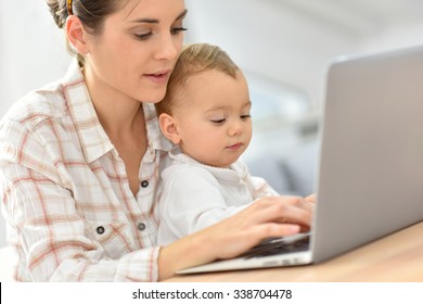 Busy young businesswoman working on laptop, baby on lap